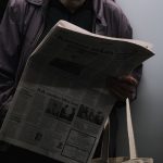A man reads a newspaper in a dimly lit public transport setting, reflecting city life. — Avast Main Reliability Options
