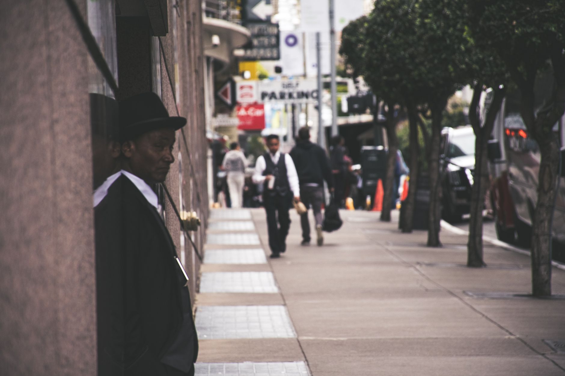 A man in a suit and hat leans against a city building, observing pedestrians. — The Hidden Mystery Behind B2B Marketing Agenc