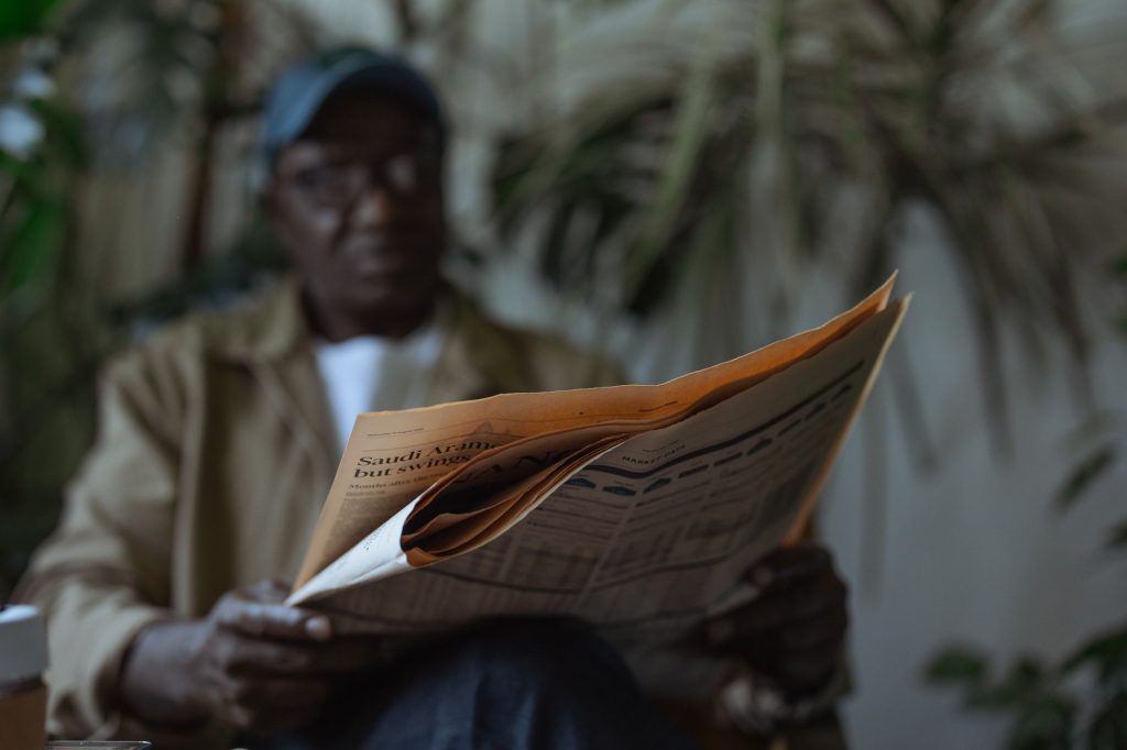 An adult man reading a newspaper indoors, surrounded by plants with a blurred background. — Vavada Bitcoin Kockanje i Njegove