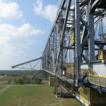 A large industrial construction machine against a blue sky and green landscape